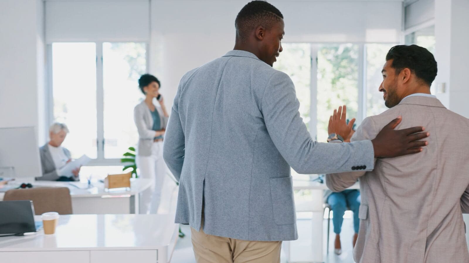 A colleague welcomed into a bright office, a hand on his shoulder